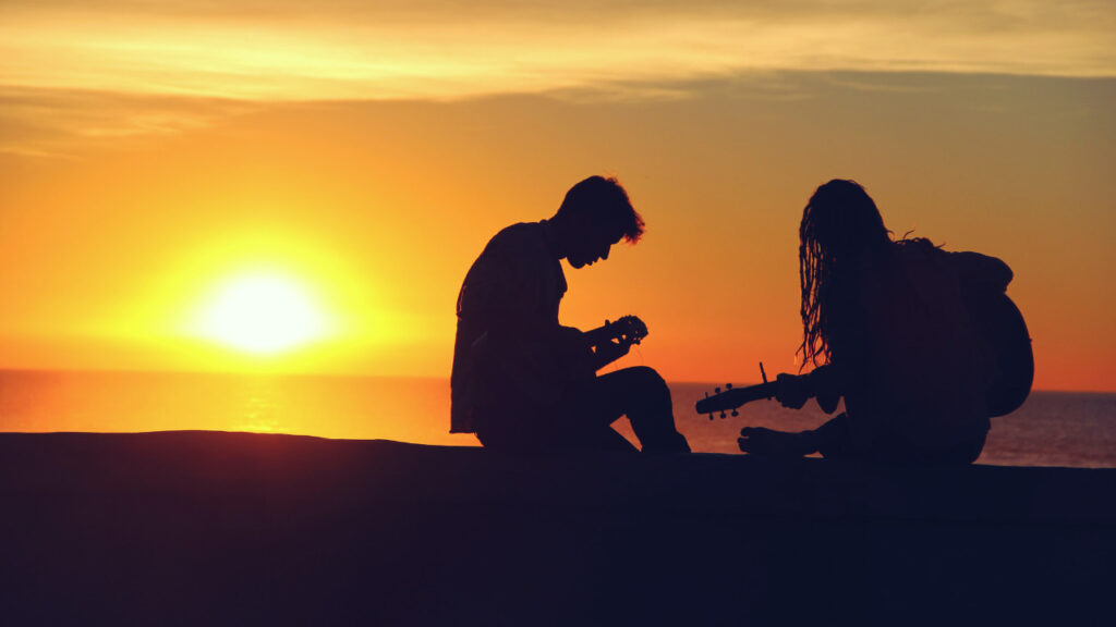 夕日をバックにギターを弾く男女